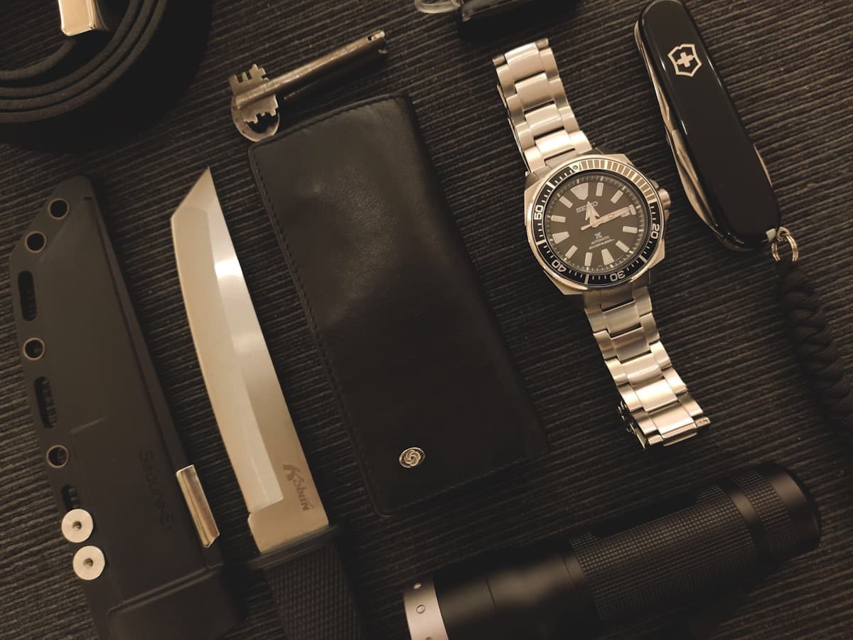 Flat lay of everyday carry gear including a knife, wallet, watch, flashlight, and multi-tool